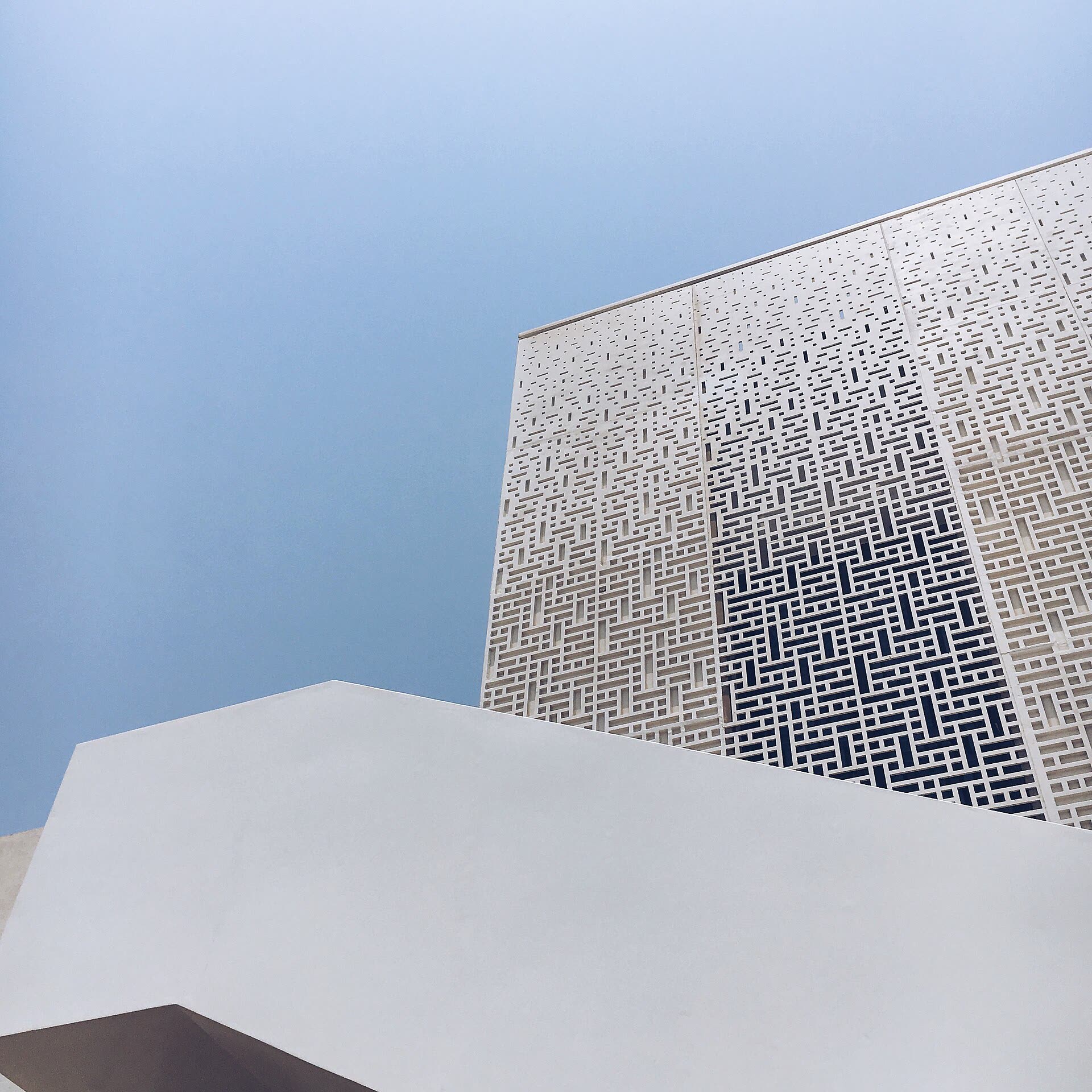 A perforated concrete screen wall meeting a plain white parapet, seen from below against an open sky.