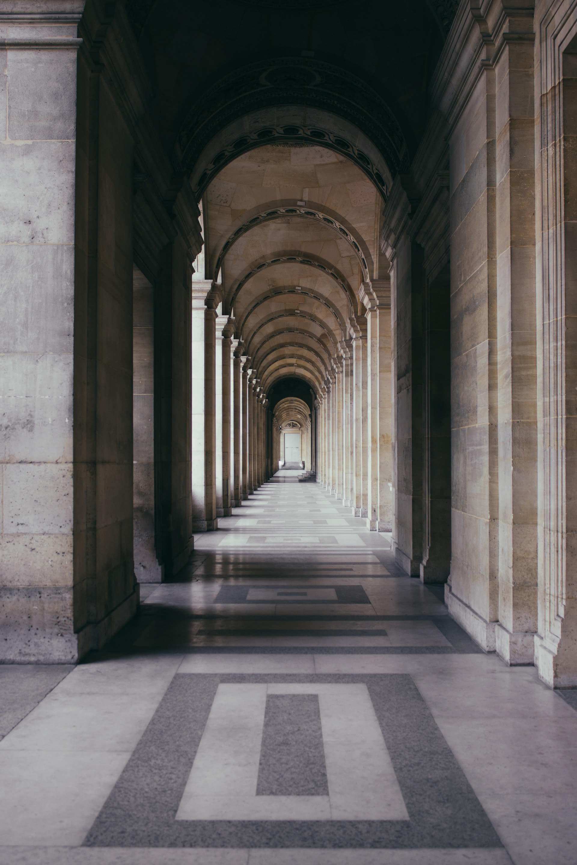 A long hallway of marble arches receding into shadow, each arch framing the next.