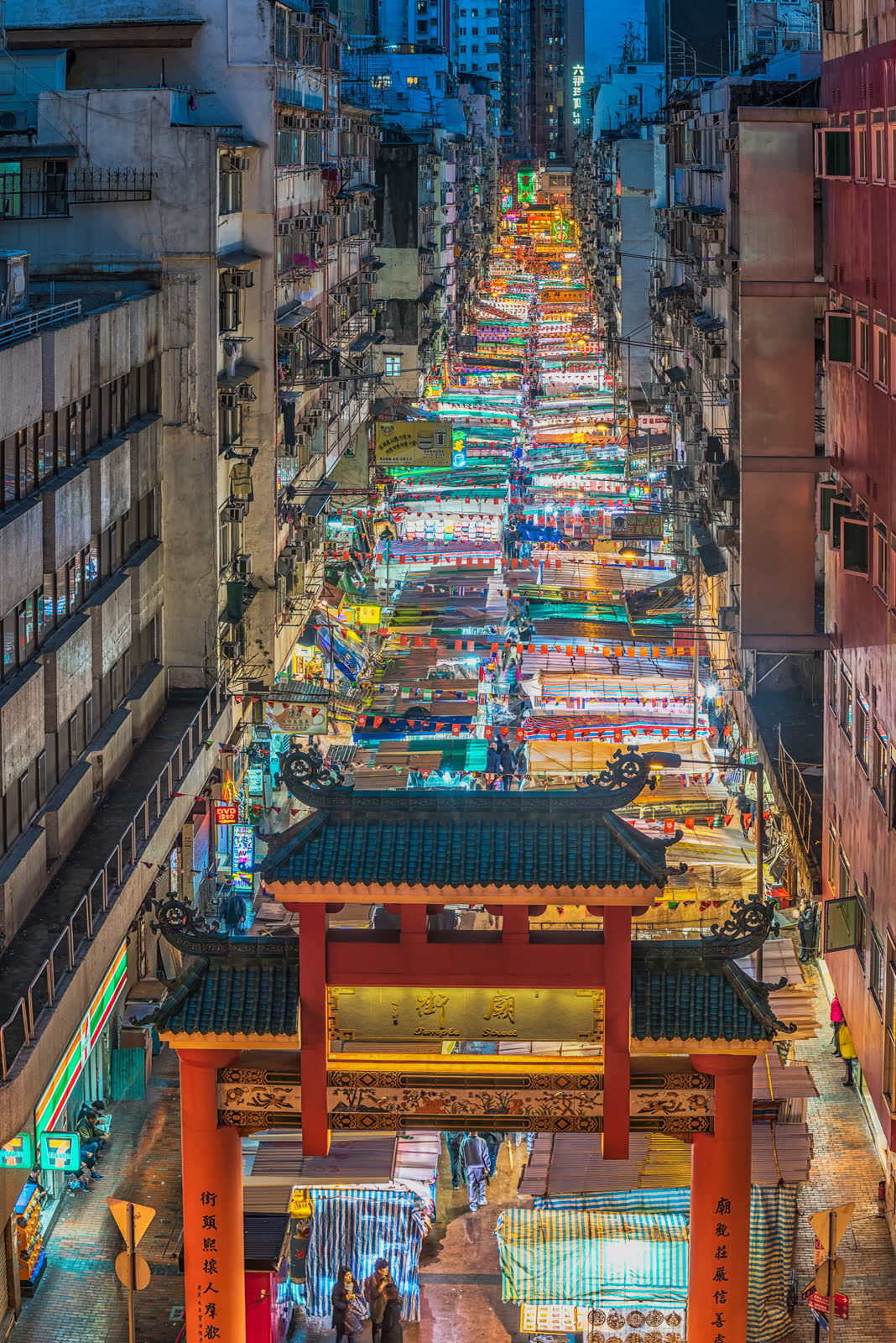 A narrow street market, awnings and hanging goods crowding a passage between shopfronts.