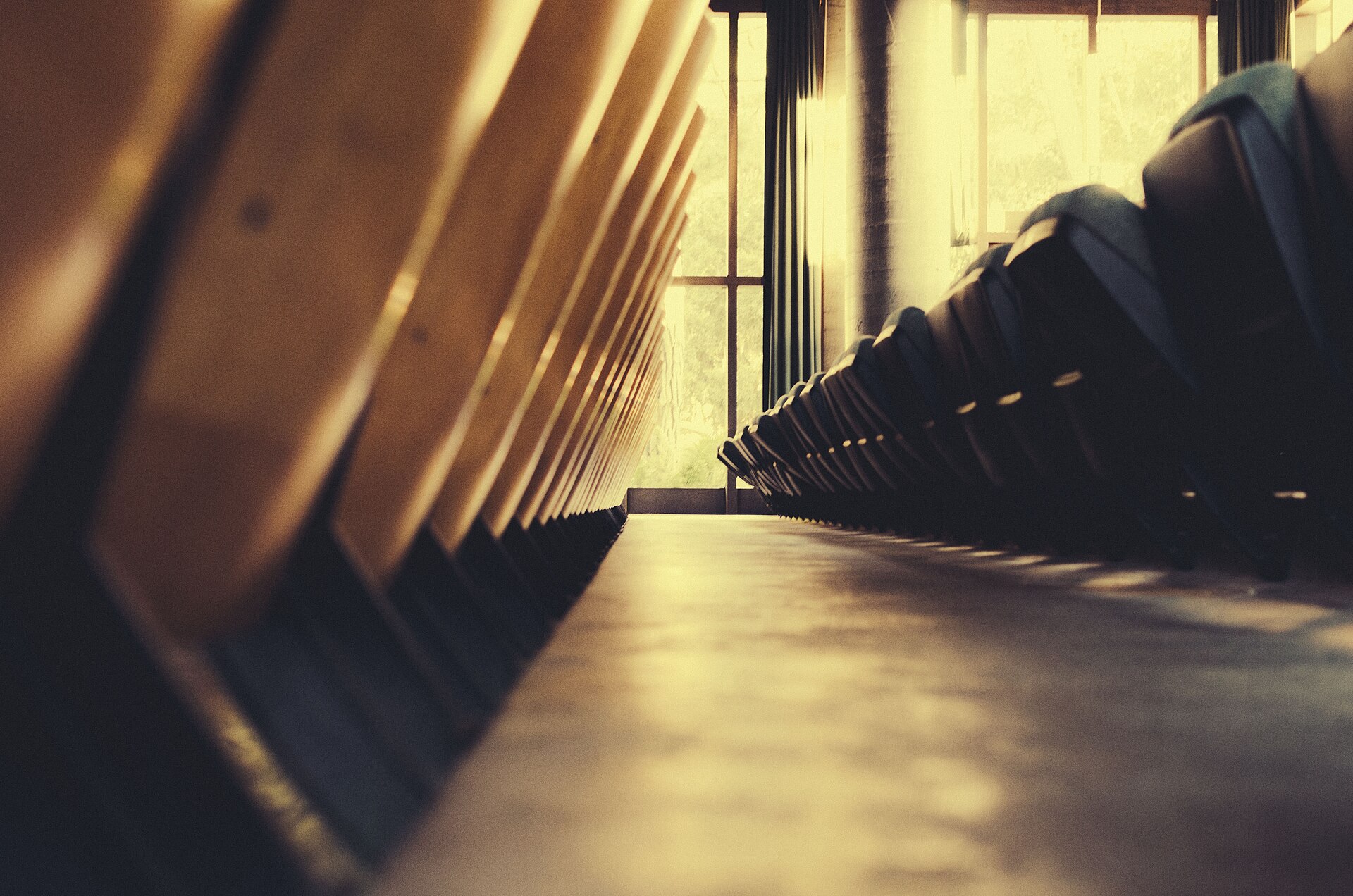 Rows of empty seats either side of an aisle in a hall, tall windows beyond, no one present.