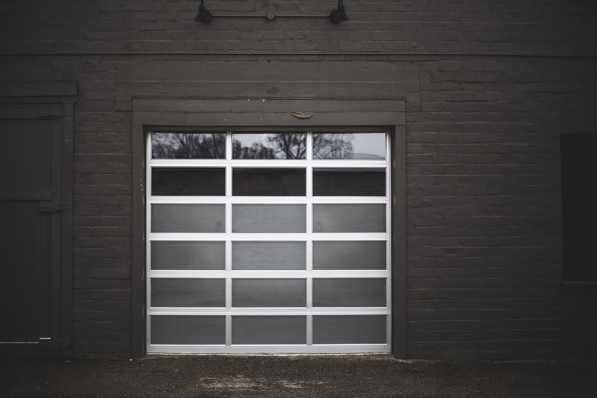 A closed sectional door with opaque glazed panels set in a dark painted brick wall, lit from behind.