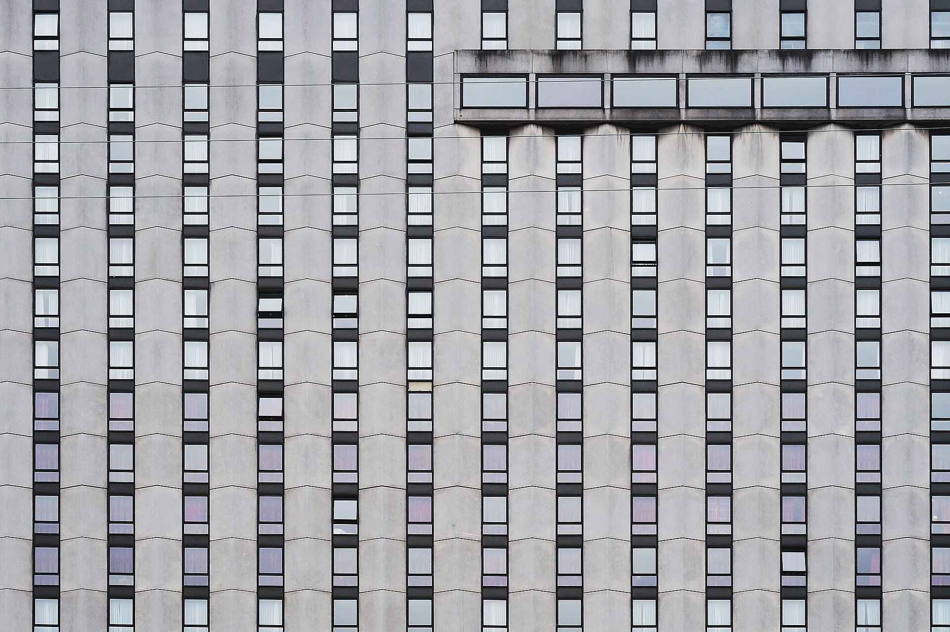 A repeating concrete facade of identical window bays, interrupted by one band of wider glazing near the top.