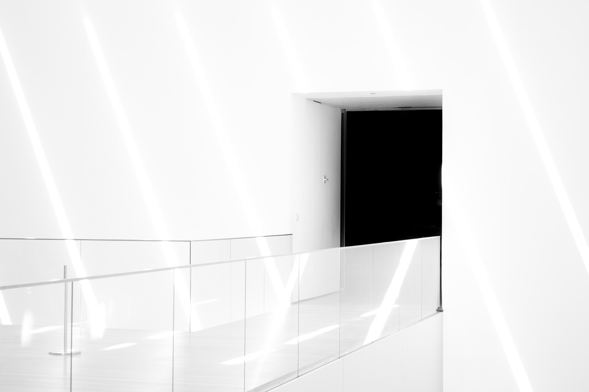 A white interior landing behind a glass balustrade, with a doorway opening onto complete darkness.
