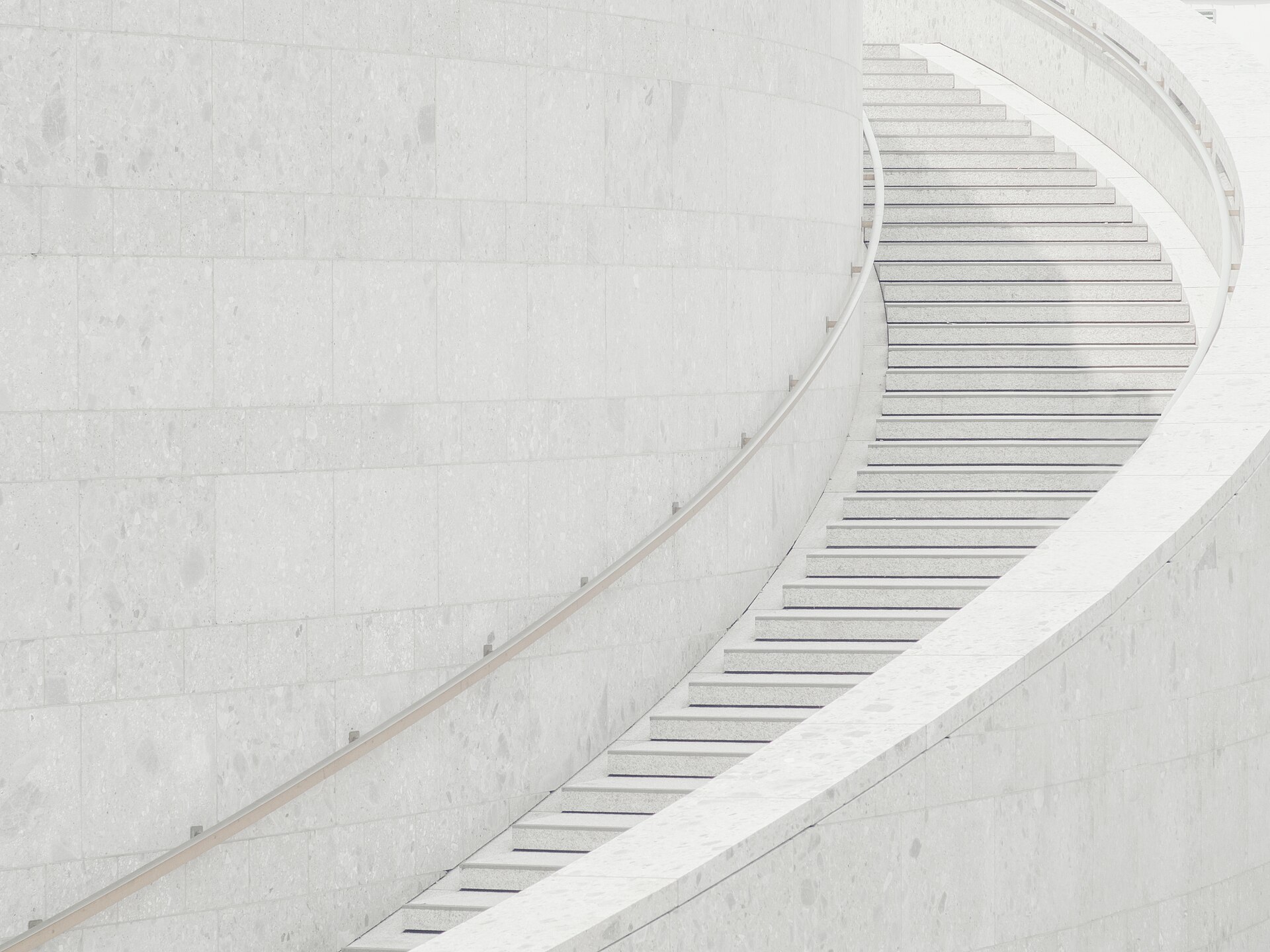 A pale stone staircase curving away against a coursed stone wall, handrail following the turn.