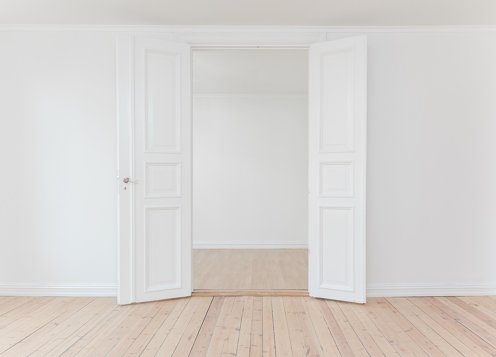 A pair of panelled double doors standing open between two empty rooms with bare boards.