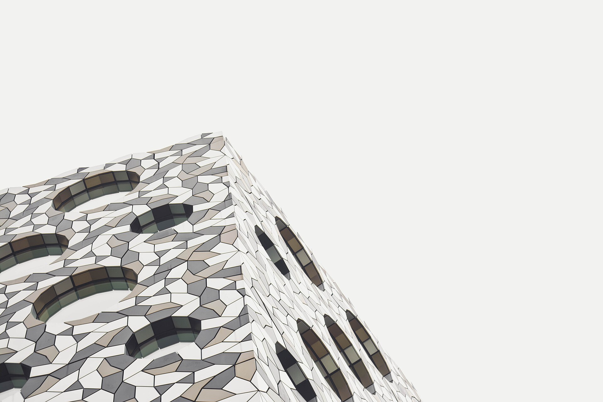 The corner of a building clad in irregular tessellated panels, set against a pale sky.