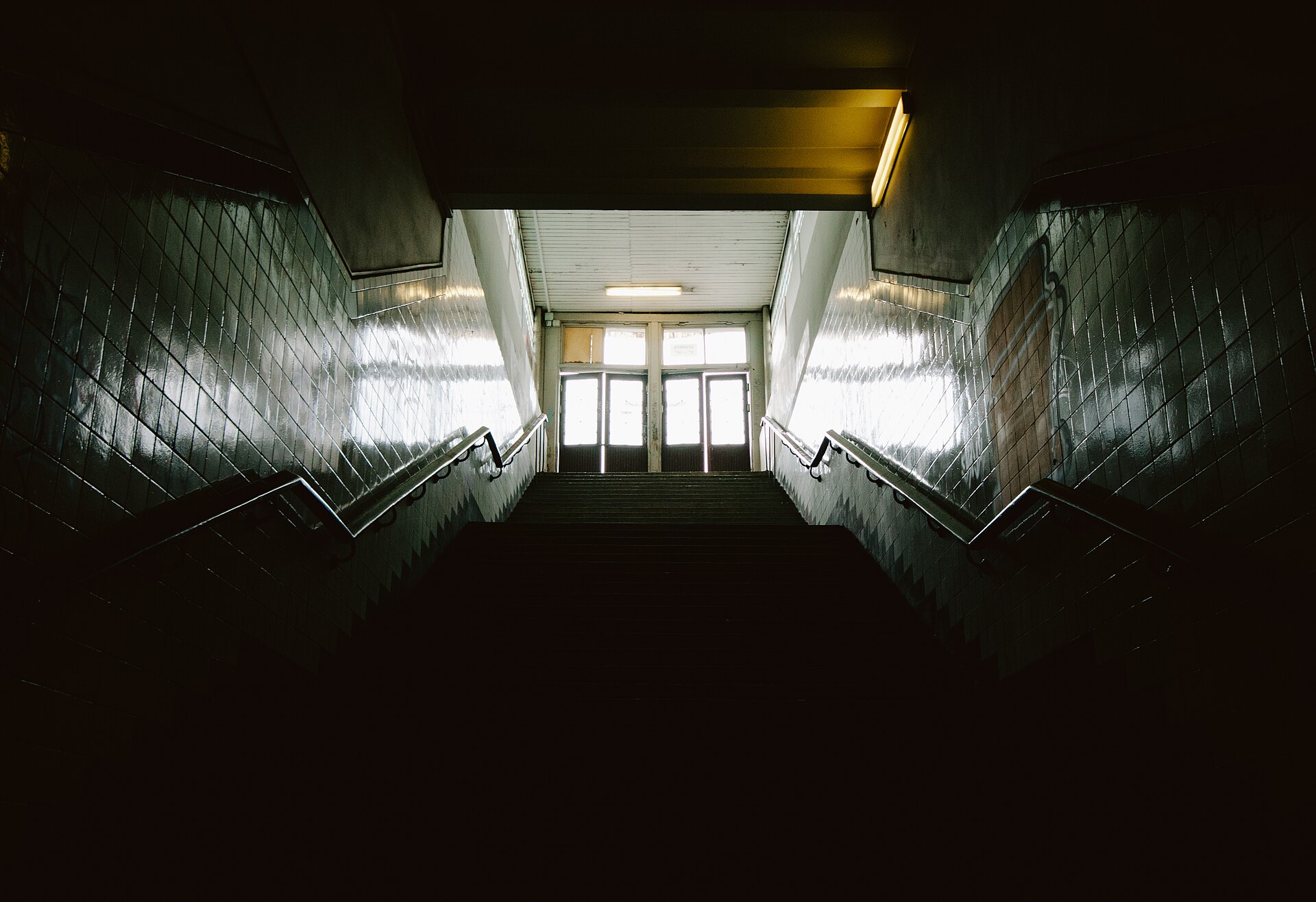 A dark tiled stairway rising towards a set of glazed doors lit from the far side.