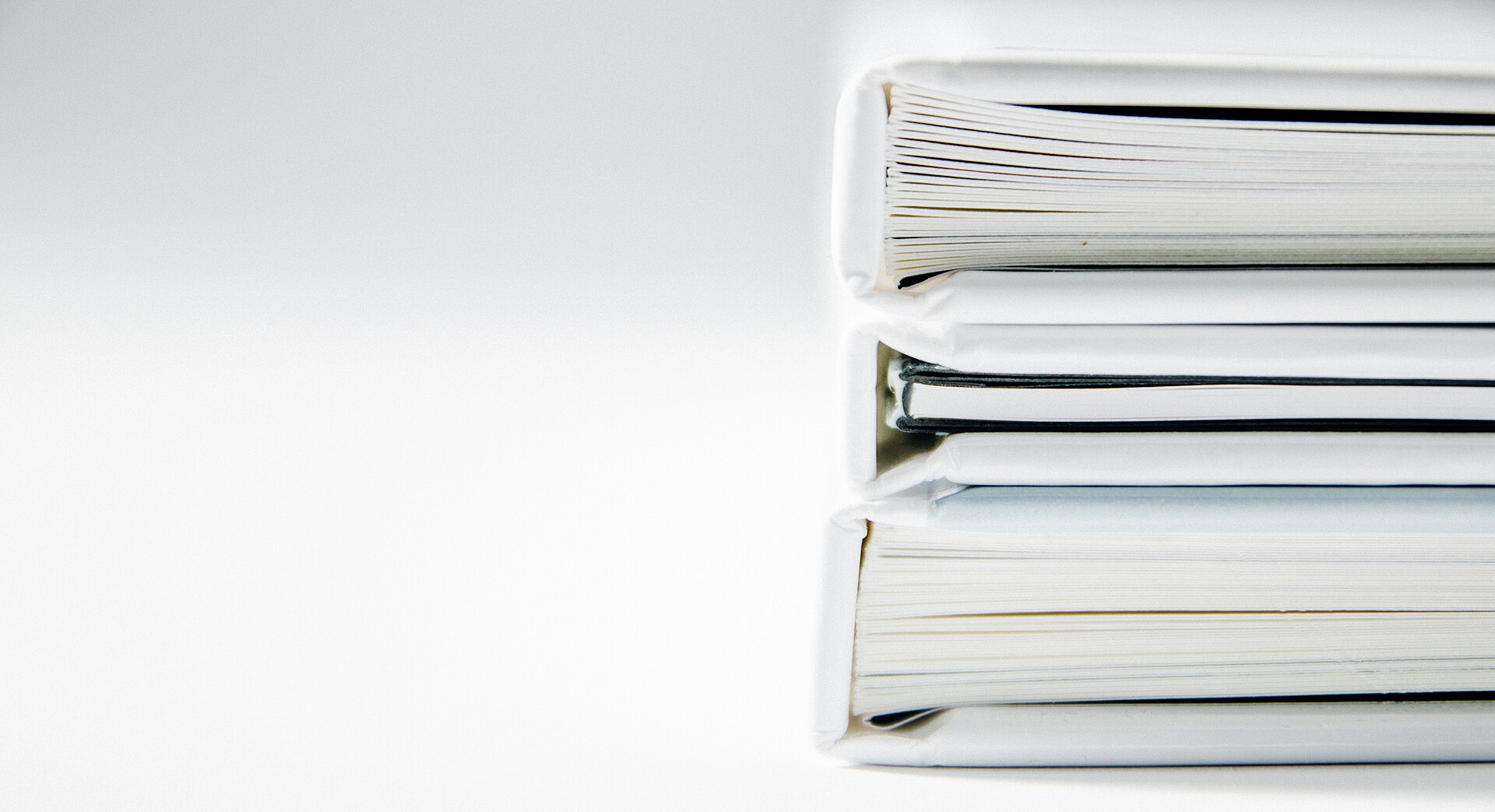 Three closed ring binders stacked on a plain surface, seen edge on, with no legible labelling.